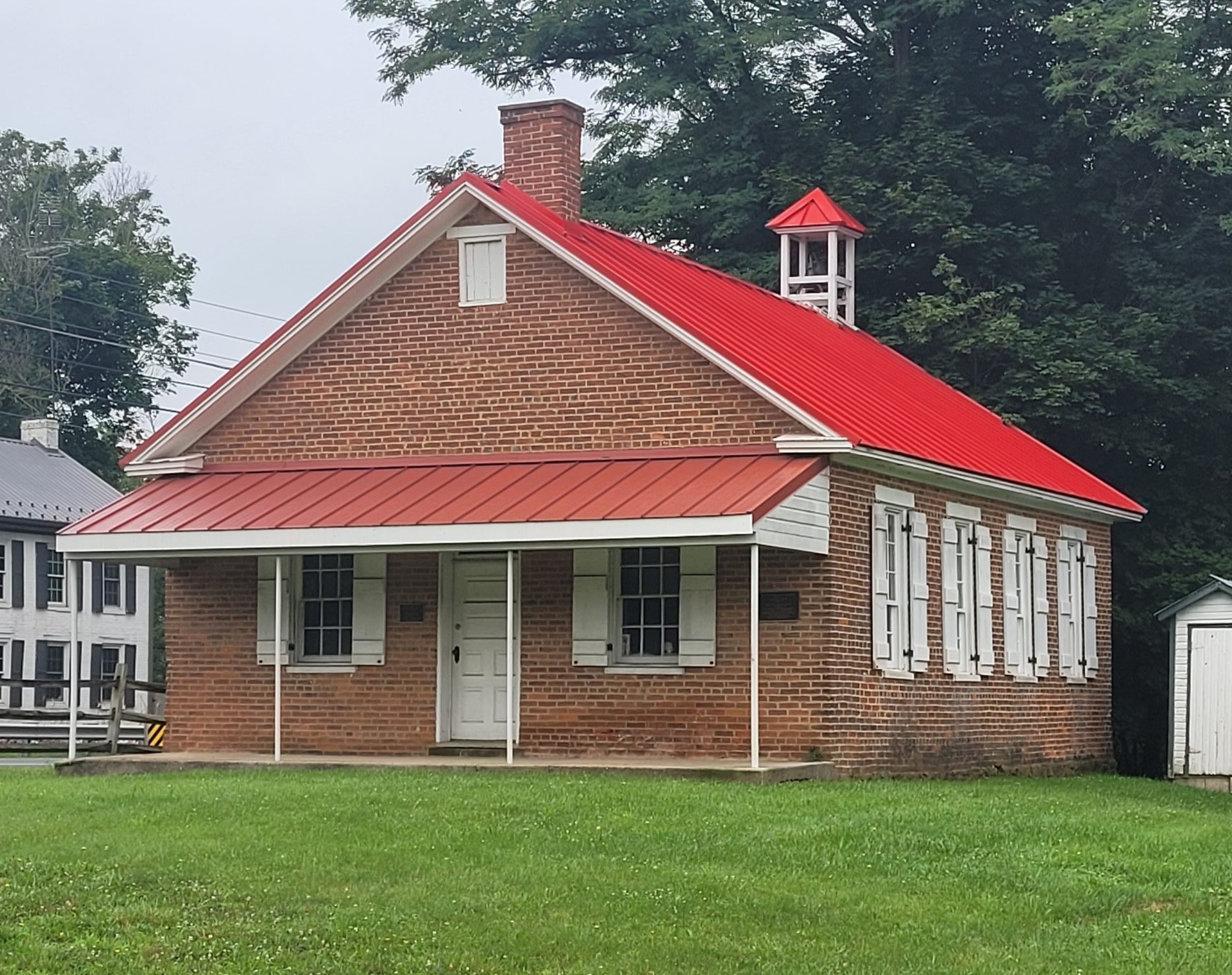 red brick single room schoolhouse with a bright red roof and white windows and doors